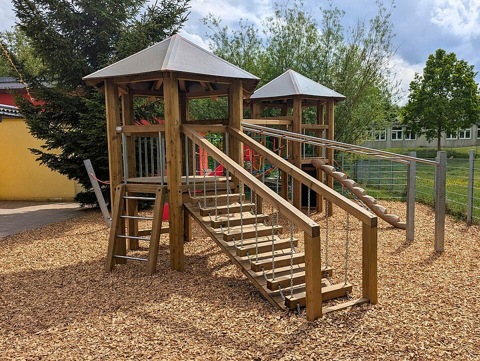 ein Klettergerüst aus Holz mit roter Rutsche im Außenbereich der Little Friends