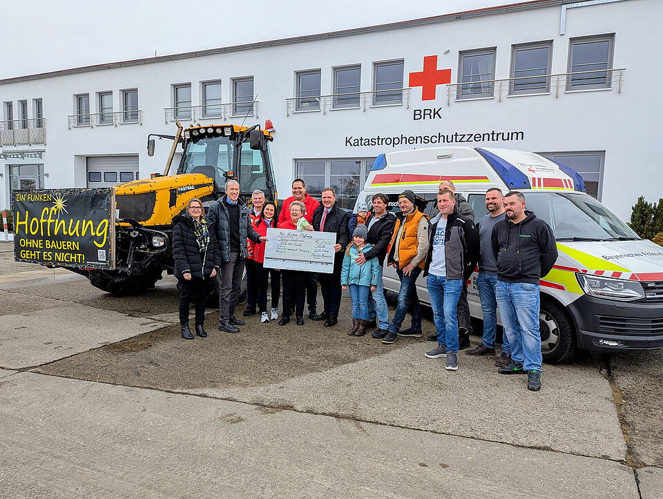 Gruppenfoto der Spendenübergabe: Christian Kammerer (6.v.r.) und Vertreter des Großhändlers OMEGA SORG überreichten im BRK-Katastrophenschutzzentrum in Atzenhof den Spendenscheck an Landrat Bernd Obst, BRK-Kreisgeschäftsführer Thomas Leipold (3. v.l.), stv. BRK-Kreisgeschäftsführerin Katrin Rohm (2.v.l.) sowie Herzenswunschinitiatorin Waltraud Heiter (5.v.l) und ihr ehrenamtliches Team., die gemeinsam vor dem Herzenswunschmobil und einem geschmückten Traktor stehen. Im Hintergrund ist das Gebäude des BRK-Katastrophenschutzzentrums in Atzenhof zu sehen.