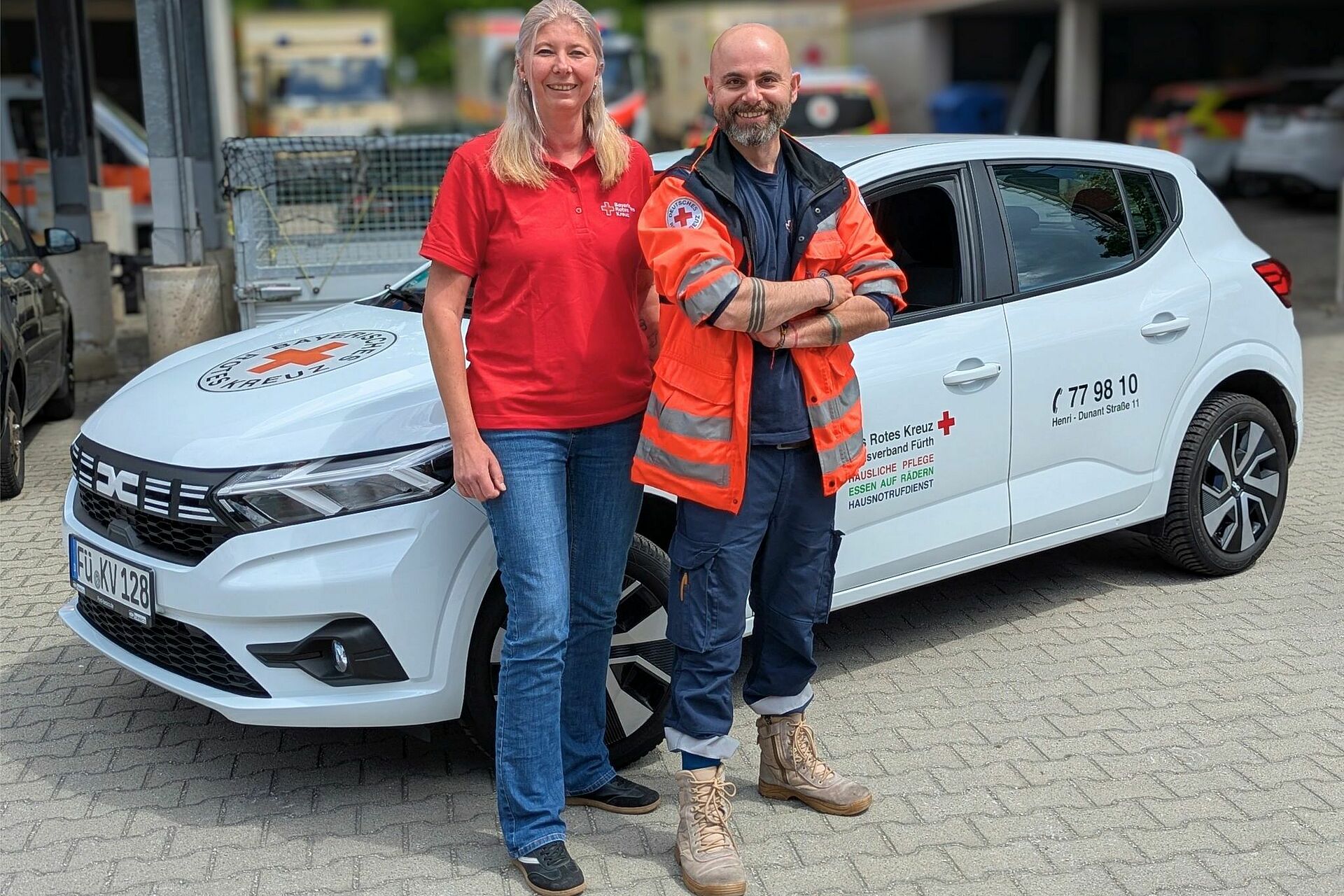 Eine Mitarbeiterin und ein Mitarbeiter der Sozialstation im BRK Fürth vor einem Einsatzauto.