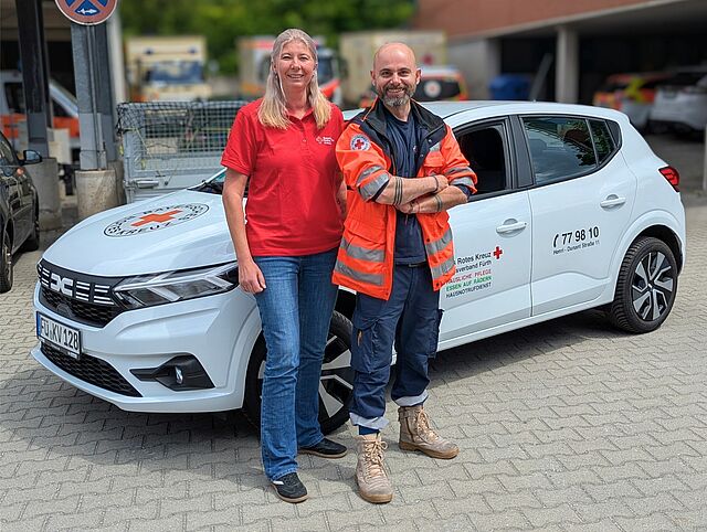 Eine Mitarbeiterin und ein Mitarbeiter der Sozialstation im BRK Fürth vor einem Einsatzauto.