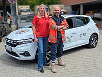 Eine Mitarbeiterin und ein Mitarbeiter der Sozialstation im BRK Fürth vor einem Einsatzauto.