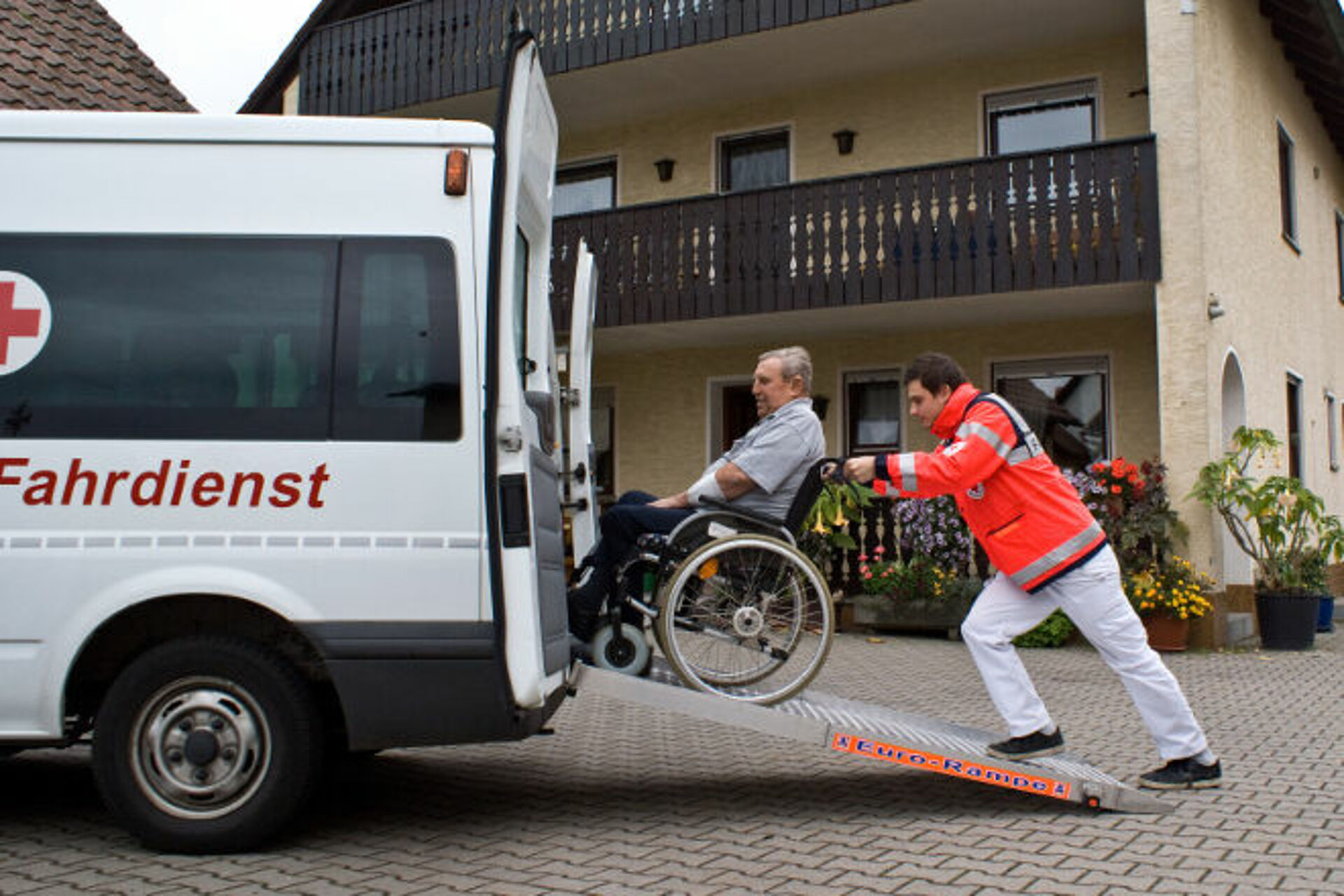 Fahrdienstmitarbeiter schiebt Mann im Rollstuhl auf Rampe in das Fahrzeug.