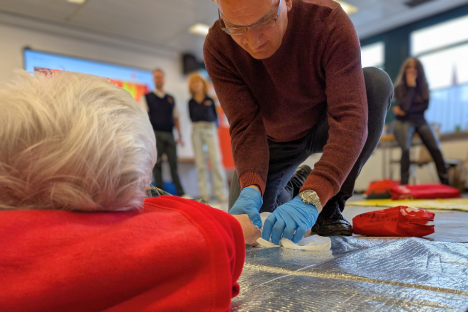 Rotkreuzkurs Erste Hilfe Szene aus einem Erste Hilfe Kurs: Nahaufnahme: Eine Mann legt einem Mann einen Verband am Arm an.