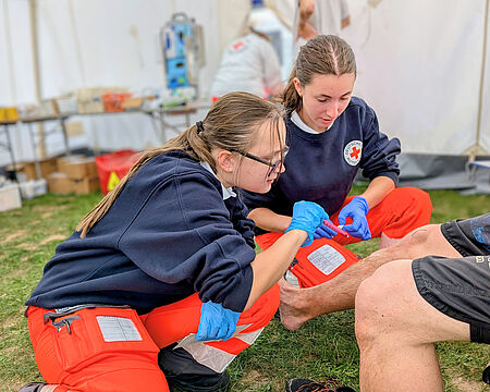 Zwei Sanitäterinnen behandeln eine Verletzung an einem Fuß.