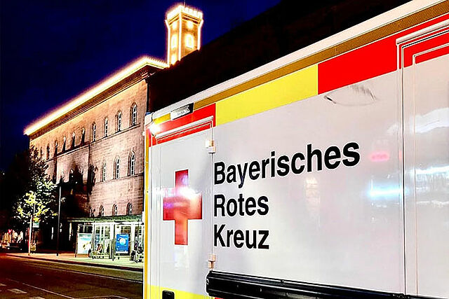 [Translate to Deutsch, leichte Sprache:] Rettungswagen vor beleuchtetem Fürther Rathaus